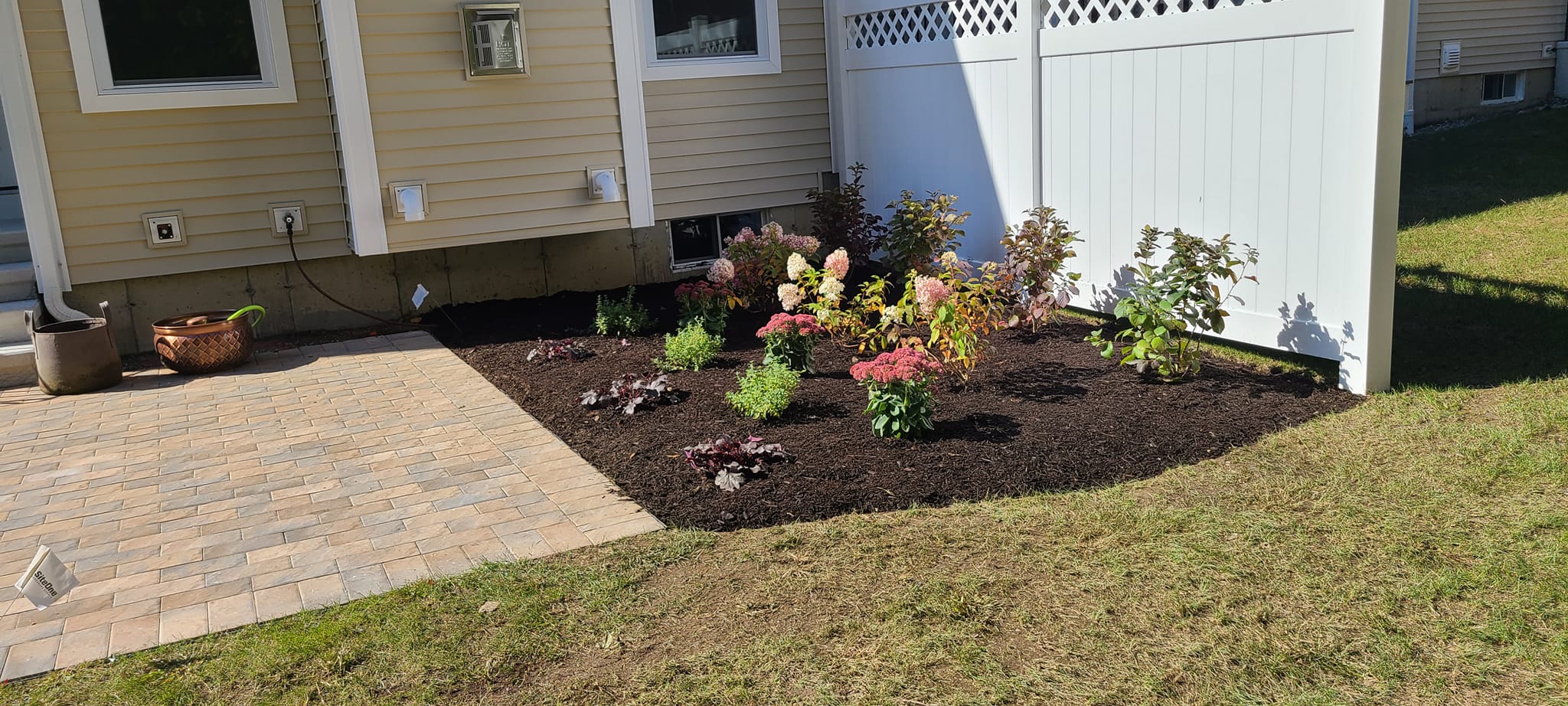 Fresh mulch bed with mixed plantings along a paver patio in Edison, NJ